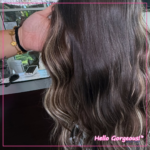 A close-up of a hand holding wavy brown hair with sparse blonde highlights at the side strands.