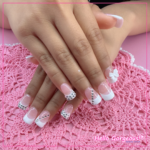 Hands showing square french-tip nails with accessories like cubic zirconia and a bow on certain fingers.