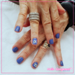 Hands showing dusty blue square nails with a hand-drawn flower accent on both ring finger nails.