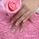 Hands showing oval french-tip nails with a sparkly silver line as an accent, on a pink backdrop, holding a rose.