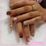 Hands showing festive nails featuring sparkly gold, red with snowflake, and red with Santa's black belt and buckle nails.