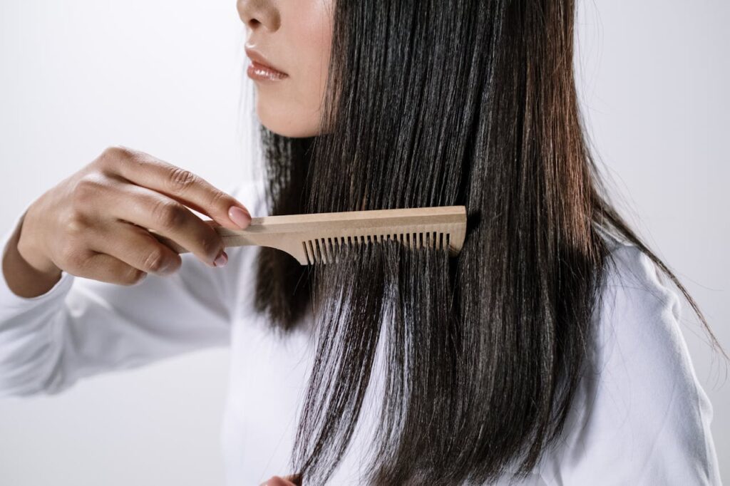 A woman brushing through her slightly thin hair with a comb.