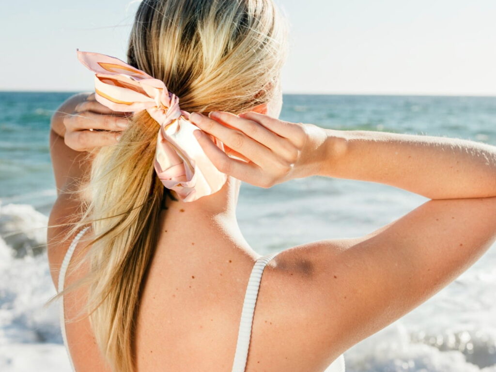Woman standing on the beach fixing the bow she has in her hair.